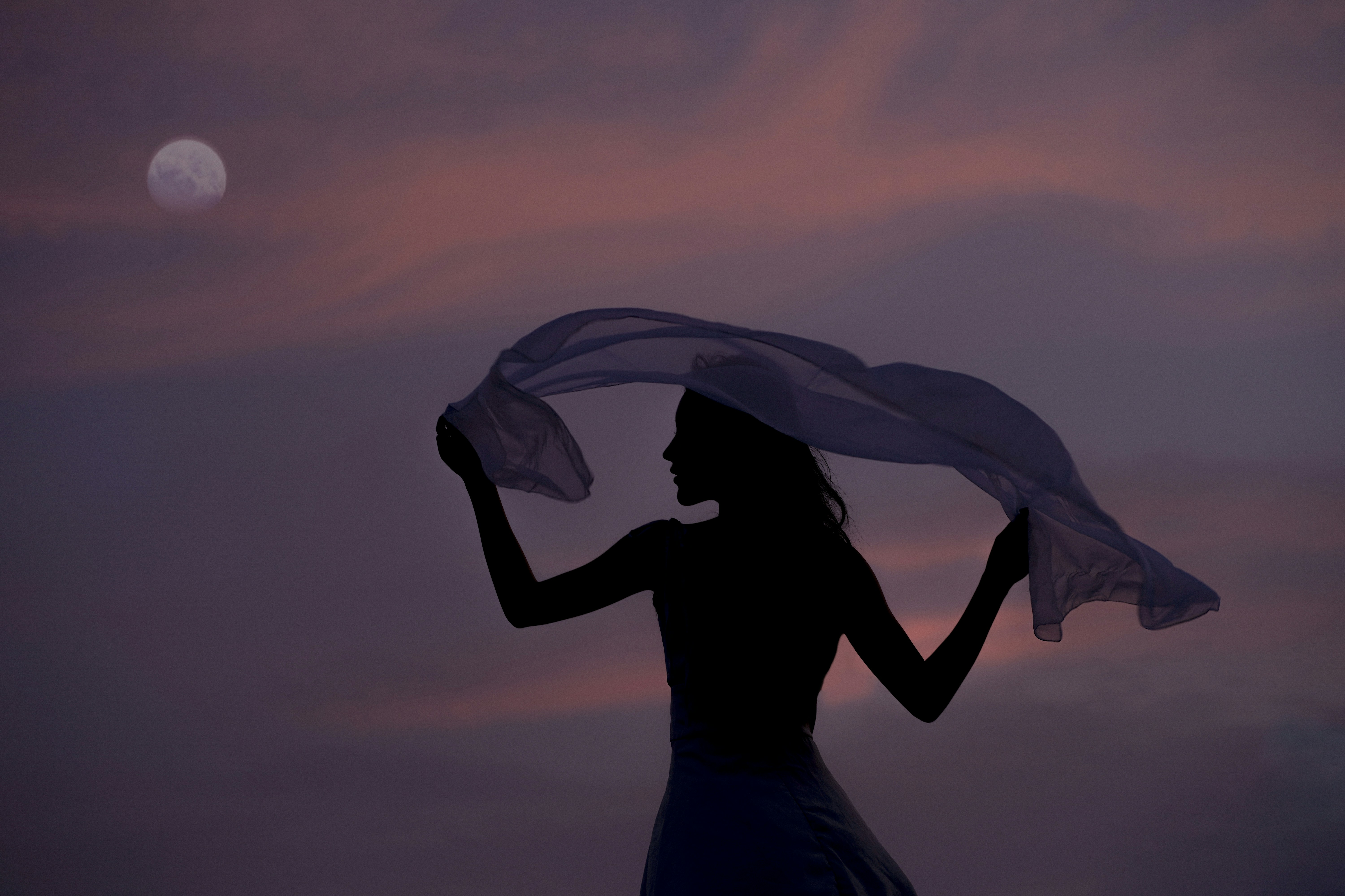  a person's silhouette against a dusk sky, holding a flowing scarf.